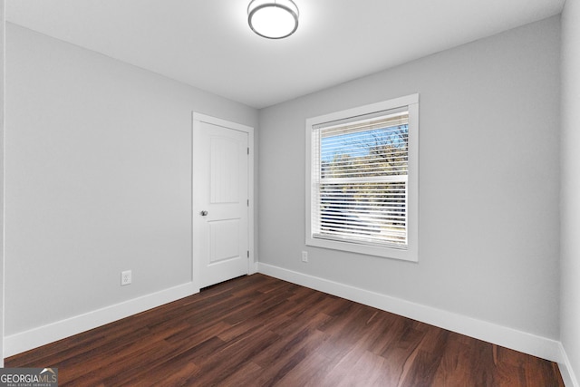 unfurnished room featuring baseboards and dark wood-style floors
