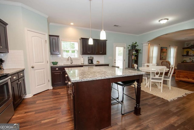 kitchen with stainless steel range with electric cooktop, arched walkways, dark brown cabinetry, a kitchen bar, and dark wood finished floors