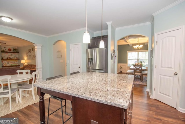 kitchen with arched walkways, stainless steel fridge, light stone counters, and dark wood finished floors