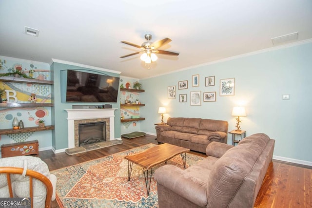 living area featuring a fireplace with raised hearth, wood finished floors, visible vents, ornamental molding, and ceiling fan