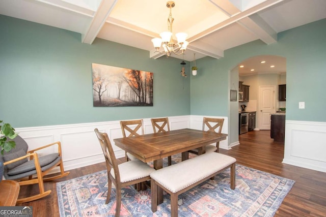 dining area with an inviting chandelier, arched walkways, dark wood-type flooring, beamed ceiling, and wainscoting
