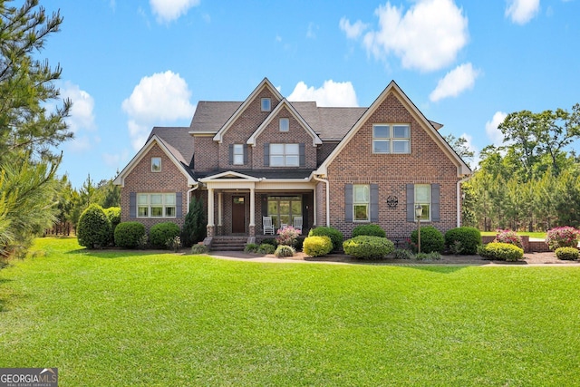 craftsman-style home featuring brick siding, covered porch, a shingled roof, and a front yard