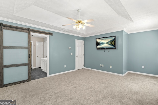 unfurnished bedroom with a raised ceiling, baseboards, dark carpet, and a barn door