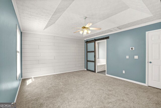 carpeted spare room with a barn door, a textured ceiling, a ceiling fan, visible vents, and ornamental molding