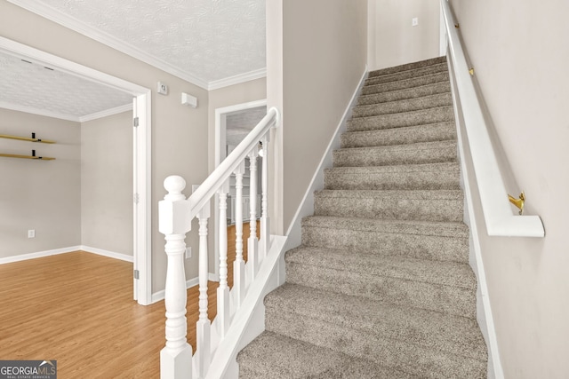 stairway featuring baseboards, a textured ceiling, crown molding, and wood finished floors