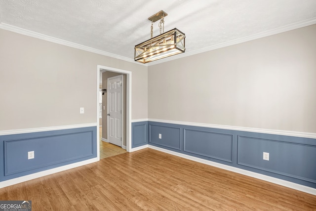 unfurnished room with ornamental molding, wood finished floors, a textured ceiling, a wainscoted wall, and a notable chandelier