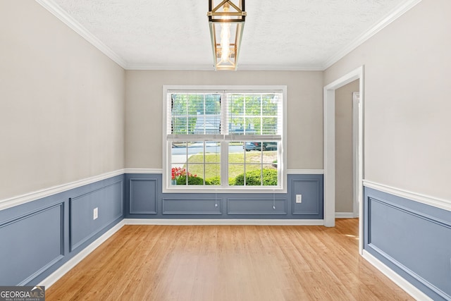 interior space featuring a textured ceiling, ornamental molding, a wainscoted wall, and light wood-style floors
