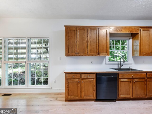 kitchen with dishwasher, a sink, light wood finished floors, brown cabinetry, and light countertops