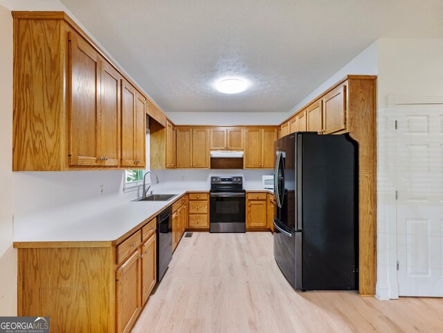 kitchen featuring black appliances, a sink, under cabinet range hood, light wood finished floors, and light countertops