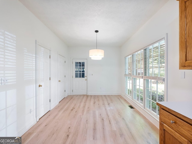 unfurnished dining area with light wood-type flooring, plenty of natural light, and baseboards