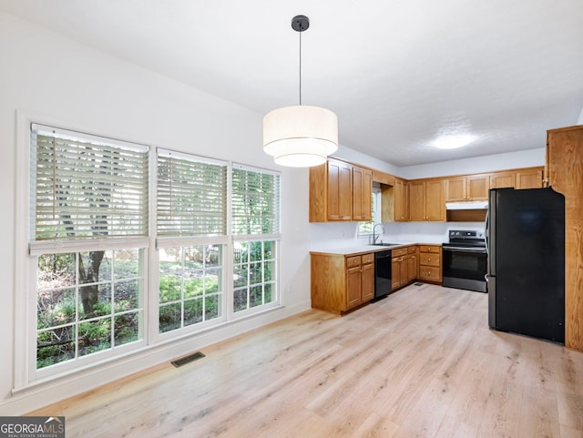 kitchen with black appliances, light wood finished floors, a sink, light countertops, and pendant lighting