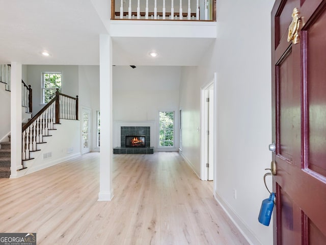 foyer entrance featuring stairs, light wood-type flooring, baseboards, a towering ceiling, and a fireplace