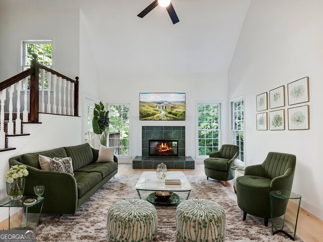 living room featuring high vaulted ceiling, wood finished floors, ceiling fan, a tile fireplace, and stairs