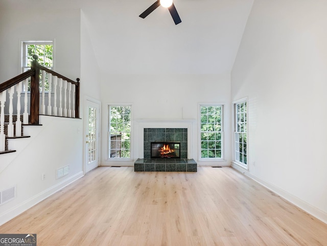 unfurnished living room with high vaulted ceiling, wood finished floors, baseboards, ceiling fan, and stairs