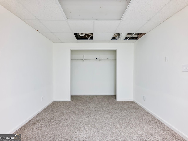 unfurnished bedroom with a drop ceiling, carpet, a closet, and baseboards