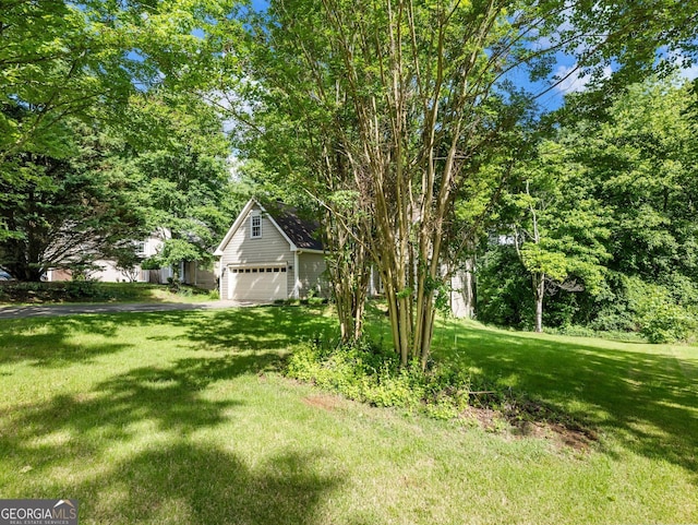 view of green lawn with a garage and asphalt driveway