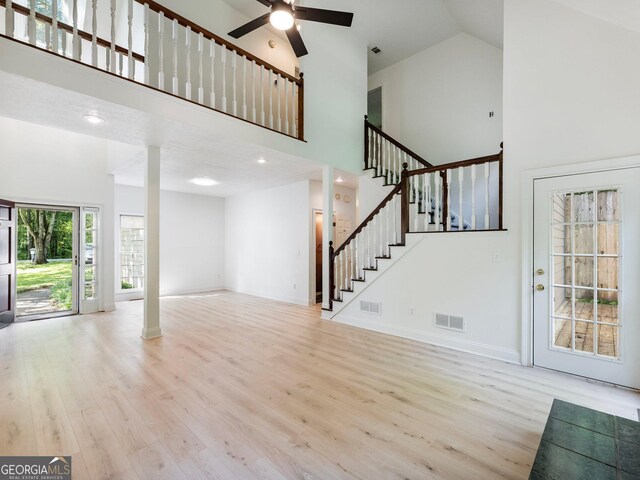 unfurnished living room featuring high vaulted ceiling, wood finished floors, ornate columns, stairway, and a ceiling fan