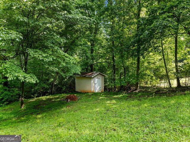 view of green lawn with a shed, an outdoor structure, and a wooded view