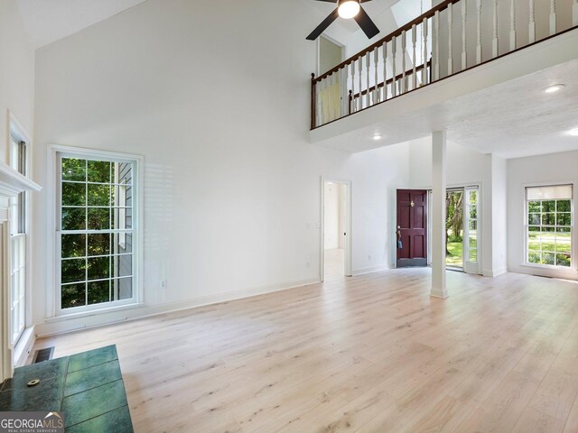 unfurnished living room with a high ceiling, ceiling fan, light wood-style floors, baseboards, and recessed lighting