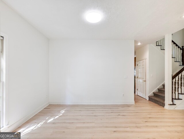 unfurnished room with light wood-style floors, stairs, and baseboards