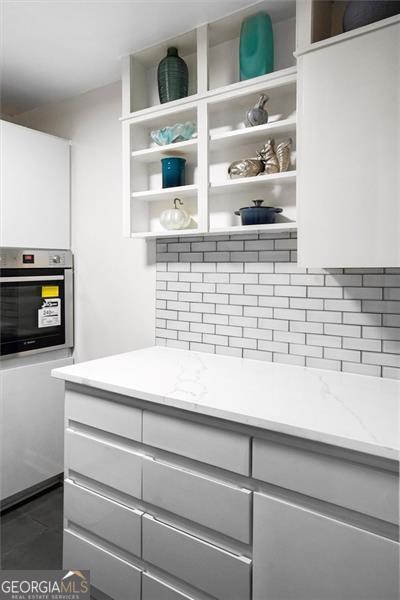 2965 Pharr Ct S Unit 110, Atlanta, GA 30305 - kitchen featuring open shelves, oven, backsplash, white cabinetry, and light stone countertops