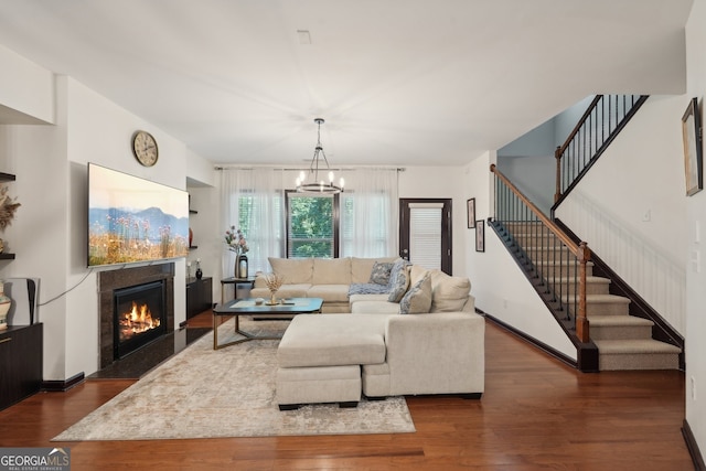 living area featuring stairway, a glass covered fireplace, an inviting chandelier, dark wood finished floors, and baseboards