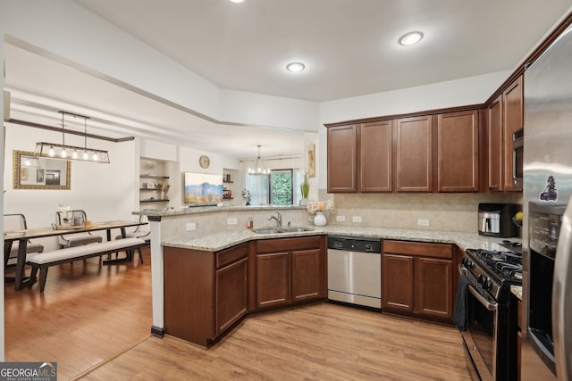 kitchen with a peninsula, a sink, a chandelier, light stone counters, and appliances with stainless steel finishes