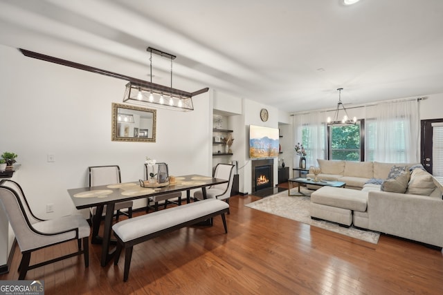 dining space featuring wood-type flooring, a fireplace with flush hearth, and an inviting chandelier