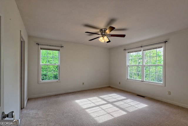 carpeted spare room featuring a ceiling fan, baseboards, visible vents, and plenty of natural light