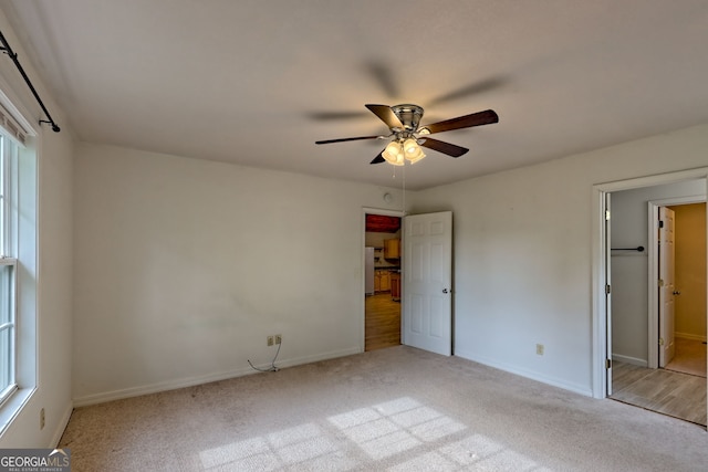 unfurnished bedroom featuring light colored carpet, freestanding refrigerator, baseboards, and ceiling fan