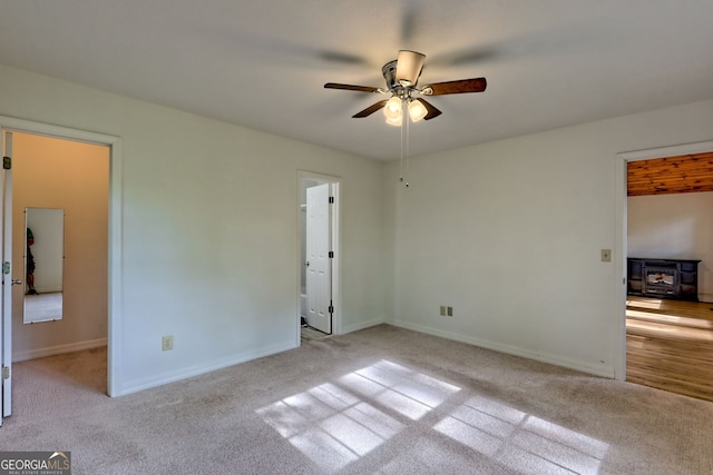 unfurnished bedroom with carpet floors, baseboards, ceiling fan, and a wood stove