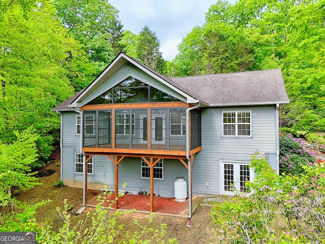 rear view of house with a sunroom, roof with shingles, and french doors
