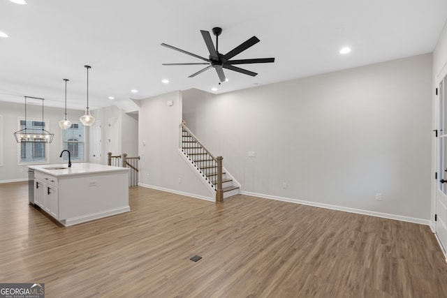 kitchen with a kitchen island with sink, light wood-style flooring, a sink, baseboards, and ceiling fan with notable chandelier