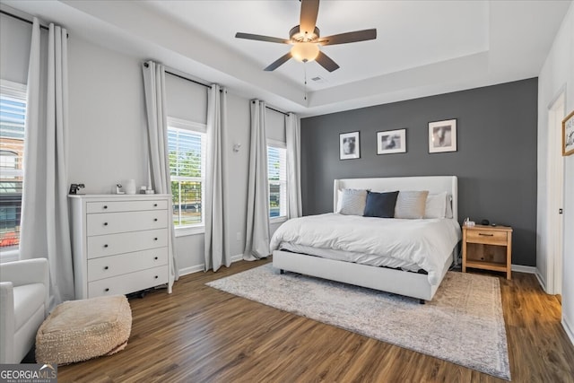 bedroom with ceiling fan, baseboards, wood finished floors, and a tray ceiling