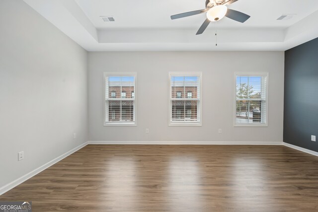 unfurnished room featuring dark wood-type flooring, a healthy amount of sunlight, a ceiling fan, and visible vents