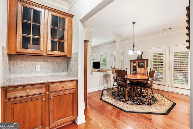 dining area with crown molding, ornate columns, a notable chandelier, and light wood-style flooring