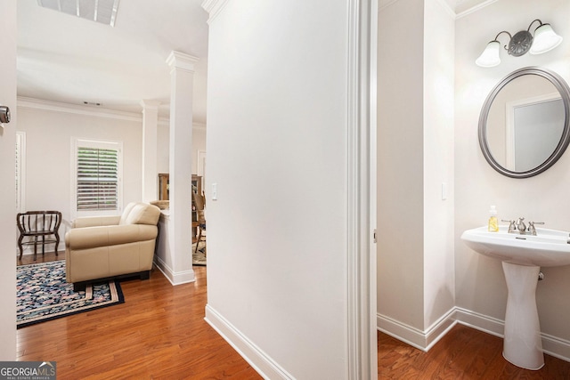 bathroom featuring crown molding, a sink, baseboards, wood finished floors, and visible vents