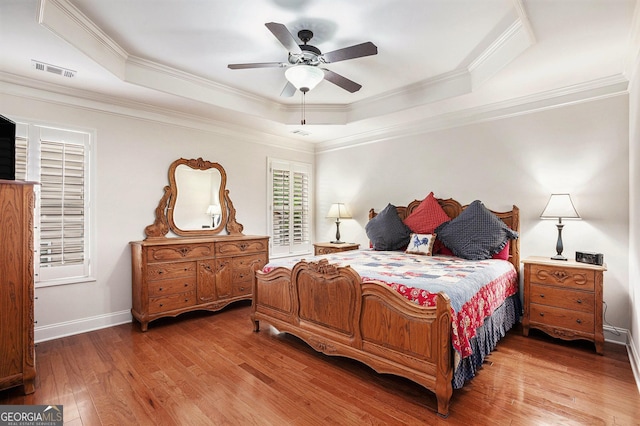 bedroom featuring visible vents, ornamental molding, wood finished floors, baseboards, and a raised ceiling