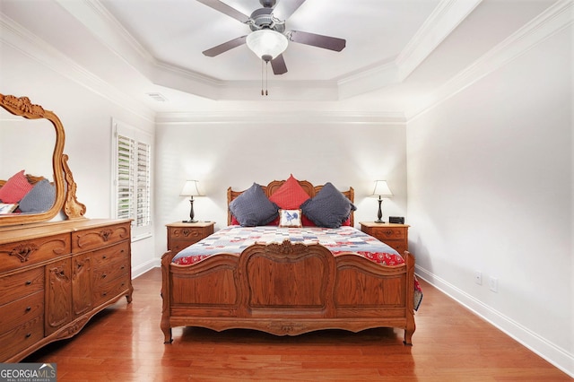 bedroom with baseboards, a tray ceiling, light wood-type flooring, and visible vents