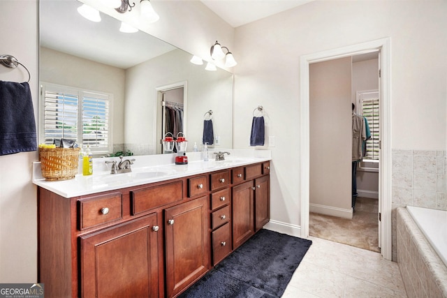 bathroom featuring double vanity, tiled tub, tile patterned flooring, a sink, and baseboards