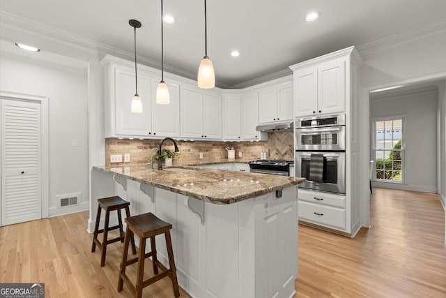 kitchen featuring a sink, stainless steel appliances, white cabinets, a kitchen bar, and light stone countertops