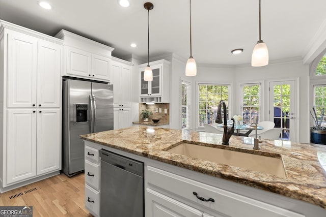 kitchen with stainless steel appliances, a sink, white cabinets, ornamental molding, and light stone counters