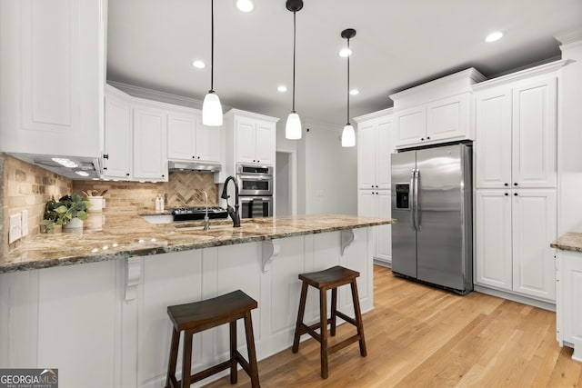 kitchen with appliances with stainless steel finishes, a peninsula, under cabinet range hood, white cabinets, and tasteful backsplash