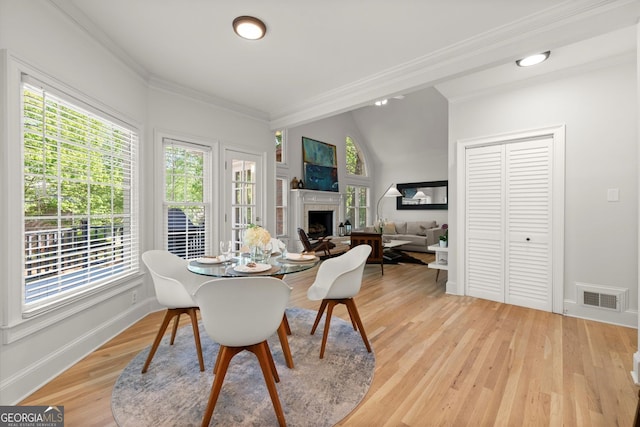 dining area featuring a fireplace, healthy amount of natural light, crown molding, and light wood-type flooring