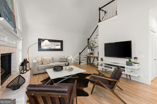 living area with a towering ceiling, light wood-style floors, a fireplace, and stairs