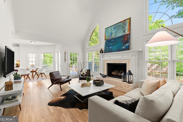 living room featuring high vaulted ceiling, plenty of natural light, wood finished floors, and a brick fireplace