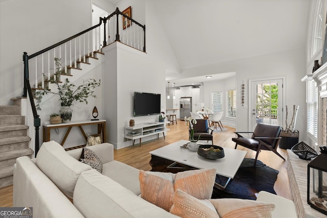 living room featuring stairway, light wood-style floors, high vaulted ceiling, and baseboards