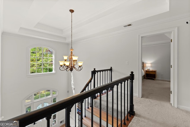 hallway featuring a tray ceiling, a chandelier, light colored carpet, ornamental molding, and an upstairs landing