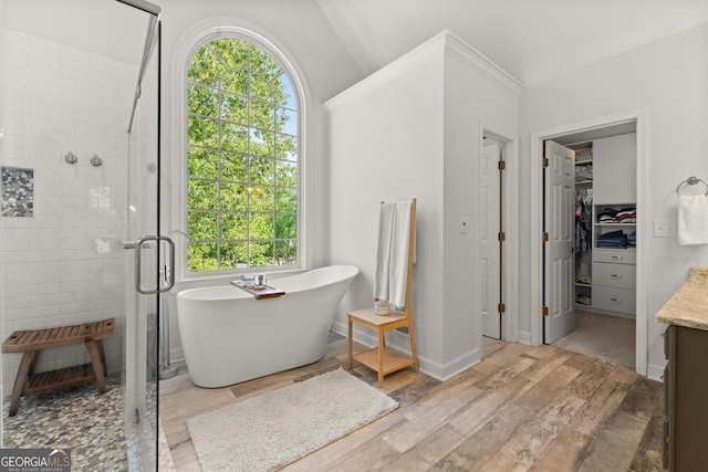 bathroom with a stall shower, wood finished floors, a soaking tub, a walk in closet, and vanity