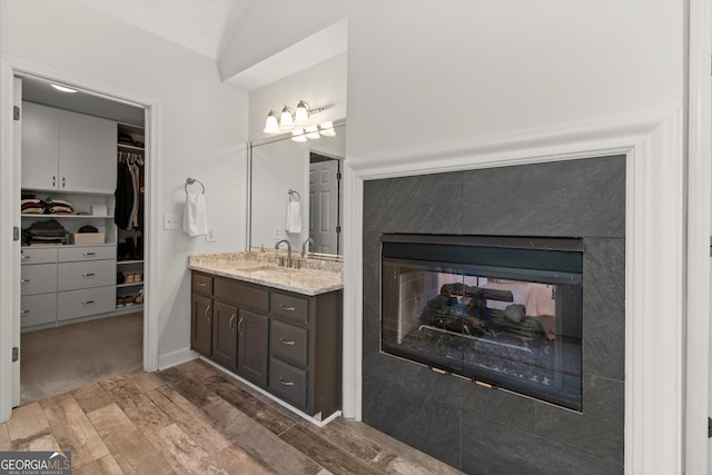 bathroom with vanity, wood finished floors, a walk in closet, a premium fireplace, and lofted ceiling